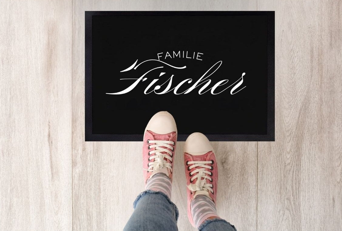  Schwarze Fußmatte mit elegantem weißen Schriftzug „Familie Fischer“ und roten Schuhen davor