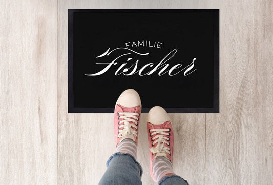  Schwarze Fußmatte mit elegantem weißen Schriftzug „Familie Fischer“ und roten Schuhen davor