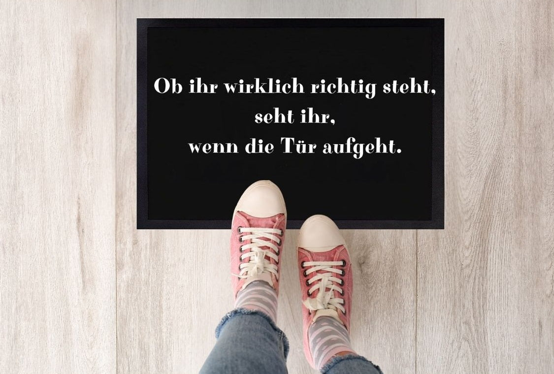 Schwarze Fußmatte mit dem weißen Spruch „Ob ihr wirklich richtig steht...“ und zwei Füßen davor