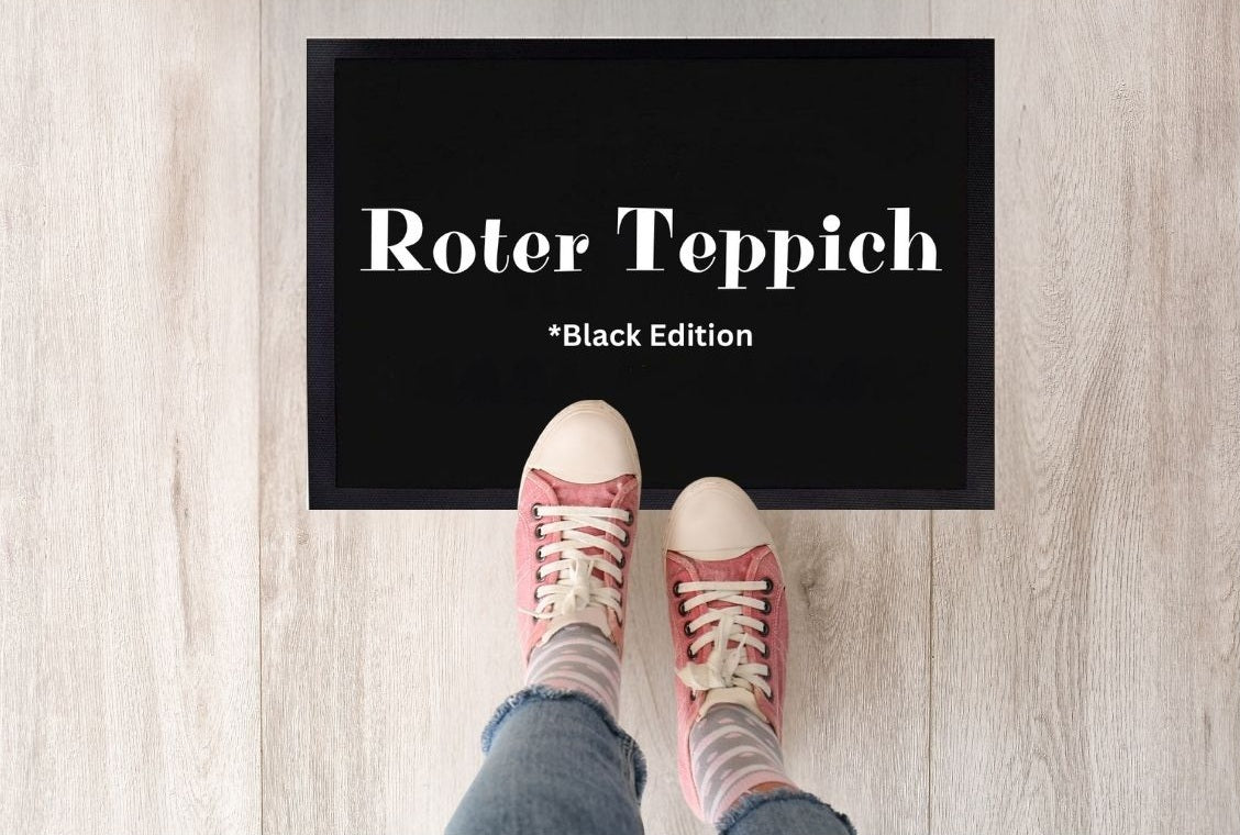  Schwarze Fußmatte mit weißer Aufschrift „Roter Teppich – Black Edition“, fotografiert von oben mit zwei Schuhspitzen davor