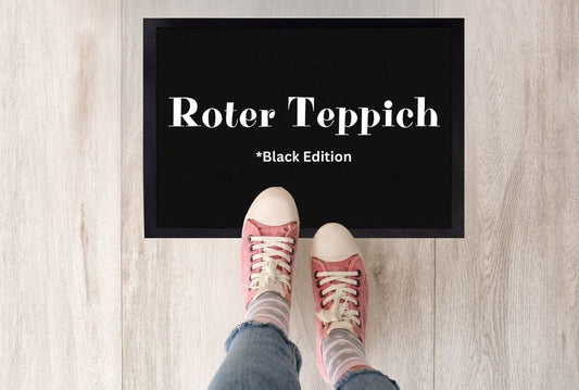  Schwarze Fußmatte mit weißer Aufschrift „Roter Teppich – Black Edition“, fotografiert von oben mit zwei Schuhspitzen davor